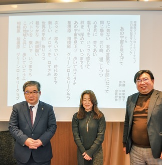 例会で歌詞が映し出されたスクリーンをバックに立つ井上さん（左）、田中さん（中央）、同ＲＣ幹事の八木美左男さん＝1月27日
