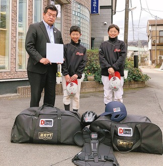 久野社長（左）に色紙を渡す宮腰さん（中央）と江成さん。手前にあるのは寄贈された野球道具＝提供