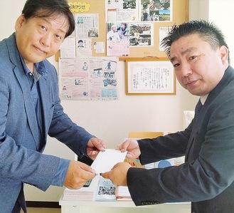同団体の井戸和宏代表理事（左）に寄付金を渡す同社の土屋健司さん