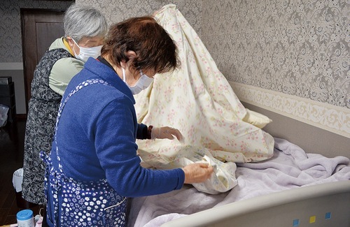 一人暮らしの高齢者のシーツ交換をする小室さん（手前）と吉澤さん