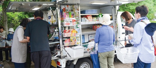 公園に設置された移動販売車で買い物する地域住民ら
