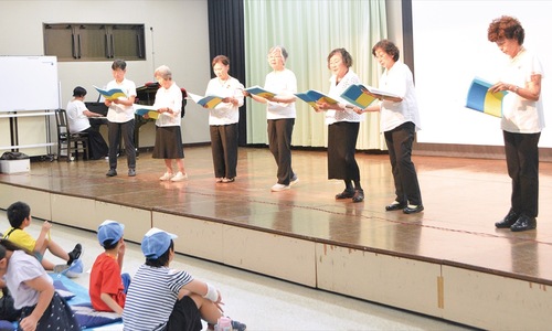 小学生の前で朗読劇を行う会員たち