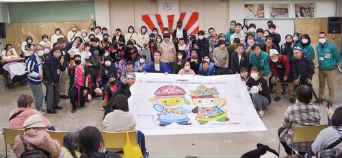 完成した巨大塗り絵と一緒に集合写真に写る同施設の利用者、職員、卒業生ら