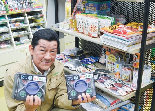 自店の｢防災・備蓄品｣陳列棚の前でスタンプを紹介する浦上代表理事