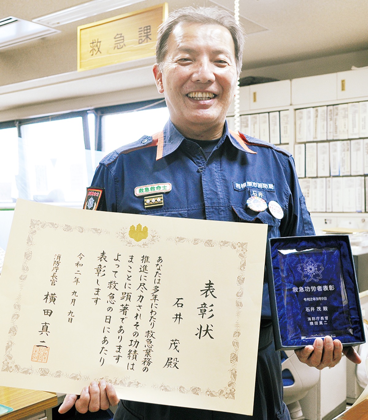 職場で賞状を手に笑顔の石井さん