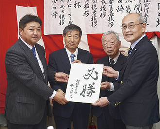 加山市長直筆の「必勝」と書かれた色紙も手渡された（左から門馬監督、大金校長、金子実行委員長、佐藤区長）