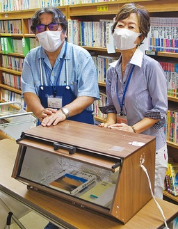 自作の図書消毒機を前に笑顔の市川勉さん（左）と図書館相武台分館の安藤康恵分館長