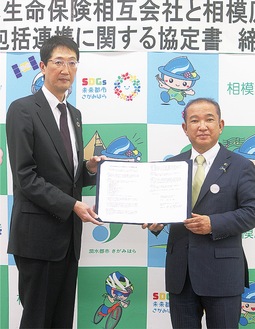 協定書を持つ本村市長と倉田支社長(左)