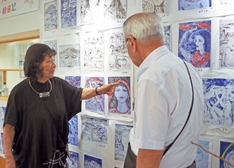 来場者にガザの画家たちからデータで送られてきた「絵日記」の説明をする上條さん（左）