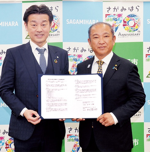 互いにサインした協定書を手にする本村市長（右）と田中社長