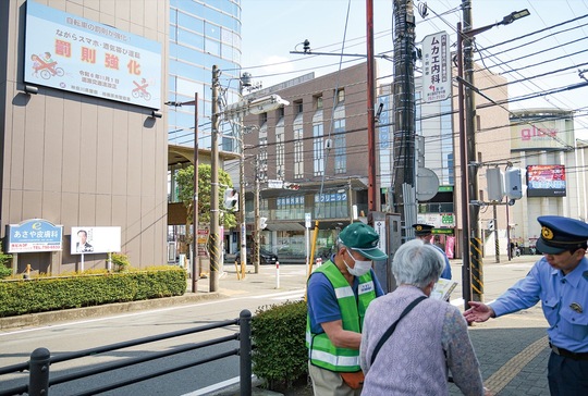 大型ビジョンのある古淵駅前交差点で啓発物を手渡す署員ら
