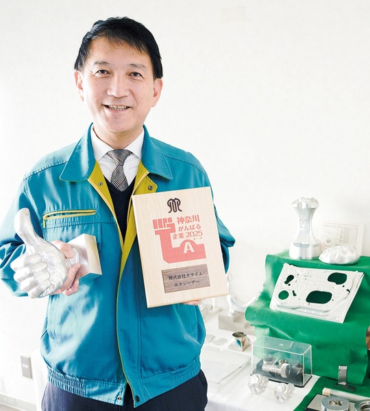 ５軸加工機で製作した「グッド」サインの加工品を手にする高橋社長