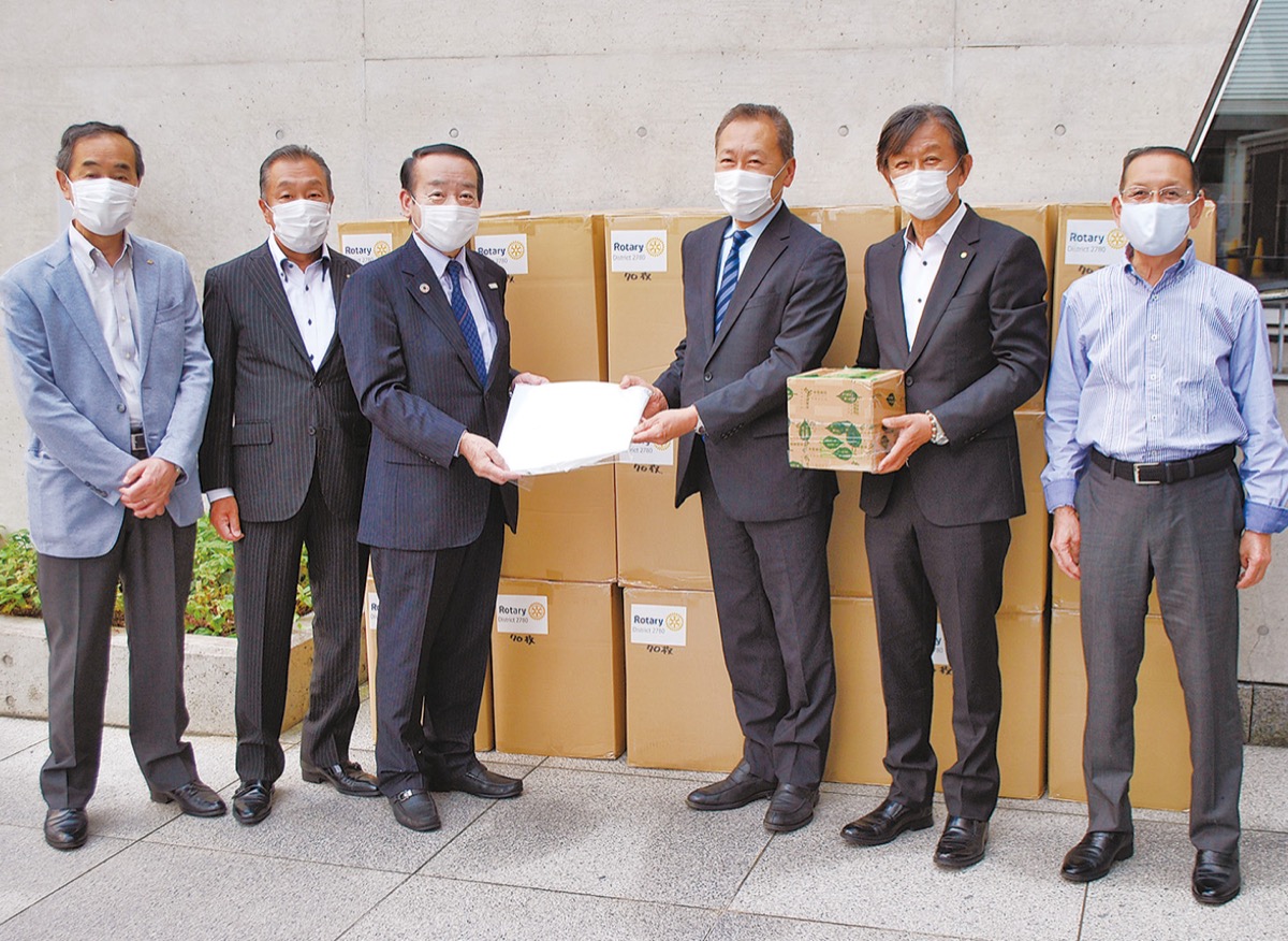 栗林ガバナー補佐（左から３人目）が代表して、土屋会長に防護服を手渡した