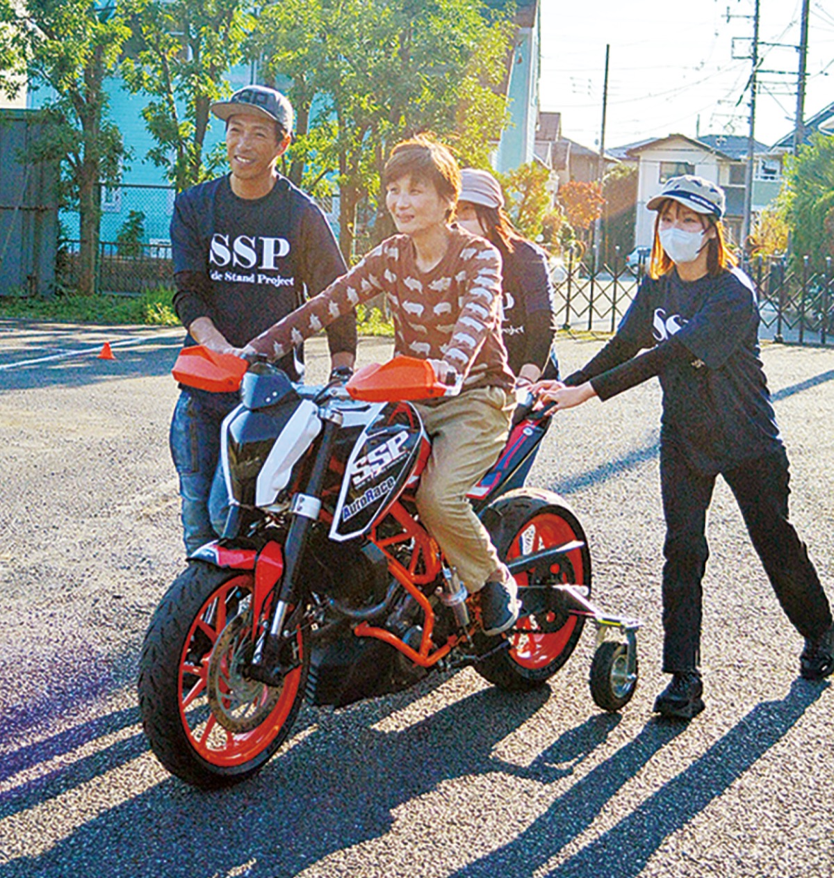 補助輪のついたバイクにまたがり笑顔の参加者と青木さん（左）