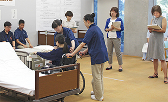 設定で右手足を麻痺した女性を介助する津久井高生徒（中央）