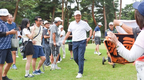 声援を受け1番ホールのティーイングエリアへ向かう原さん（中央）。18日撮影