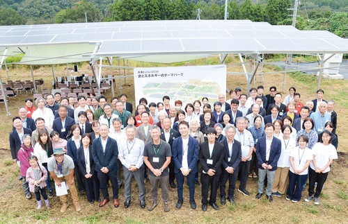 新しく完成したソーラーパネルの前で笑顔を見せる竣工式の参列者ら