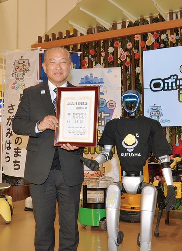 登録証を手にロボットとの撮影に応える本村市長