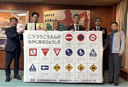 交通標識看板を手にする本村市長（左から3人目）、瓜生部長（同4人目）ら＝市提供＝