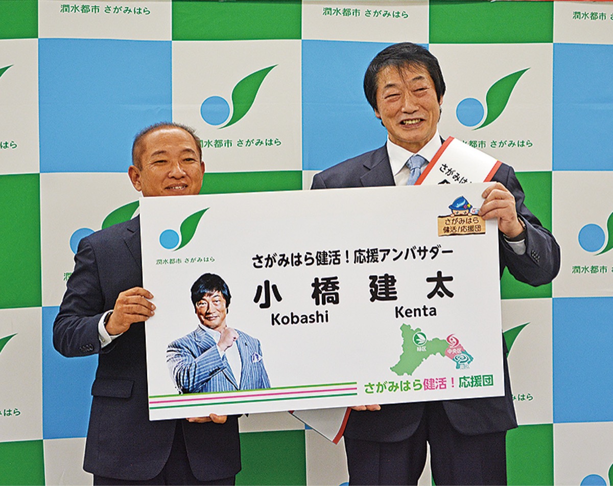 アンバサダーの名刺の拡大版を手にする小橋さん（右）と本村市長