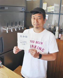 下恩方町にある高尾ビールの醸造所（おんがたブルワリー&ボトルショプ）で、創刊した冊子「たかお」を持つ池田さん