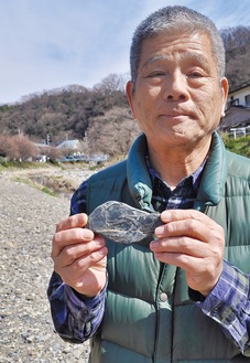 ウミユリの化石と推測する石を持つ鈴木さん。見つけた小仏川の河川敷にて＝3月17日撮影