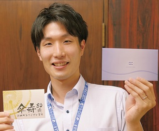 メッセージカードと粗品を持つ、市高齢者いきいき課の村田海さん