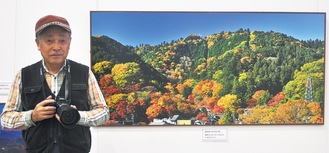先行展示している599ミュージアムで作品「東高尾山稜」（2013年）をバックにカメラを持つ樋口さん