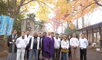 色づく紅葉の下で佐藤貫首（中央）と会員たち。左奥が観音菩薩像