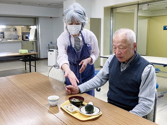 温かい朝ごはんを提供するボランティアスタッフ（左）と利用者