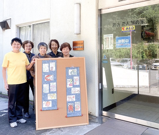 「恩方老人憩の家」の前で文化祭で展示する作品の一部を披露する絵手紙創作サークル「里の会」のメンバー