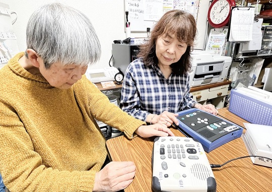 利用者が使用するCD再生機を確認する銭廣代表（左）と秦副代表