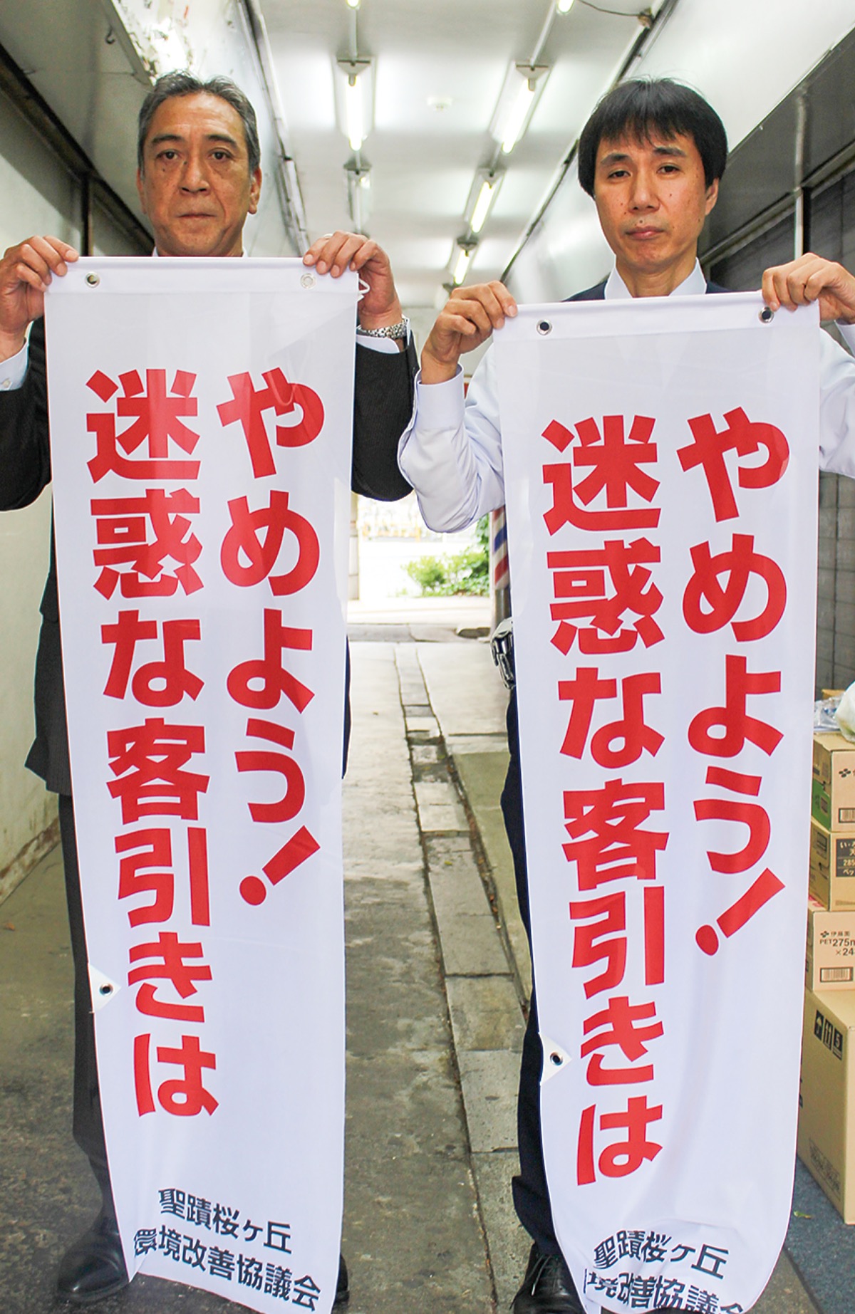 駅前に設置しているのぼりを掲げる飯島会長（左）ら