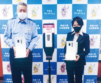 消毒液スタンドを手にする加藤署長（左）と岡田会長