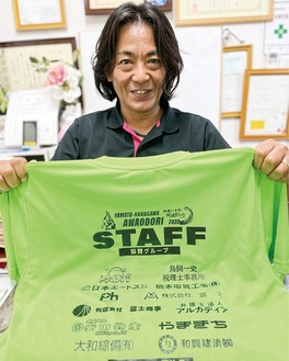 スタッフ用のシャツを手に「多くの方々のご協力に感謝します」と話す長谷川実行委員長