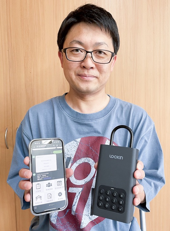 スマホとキーボックスを手に会館の予約方法を解説する家永会長