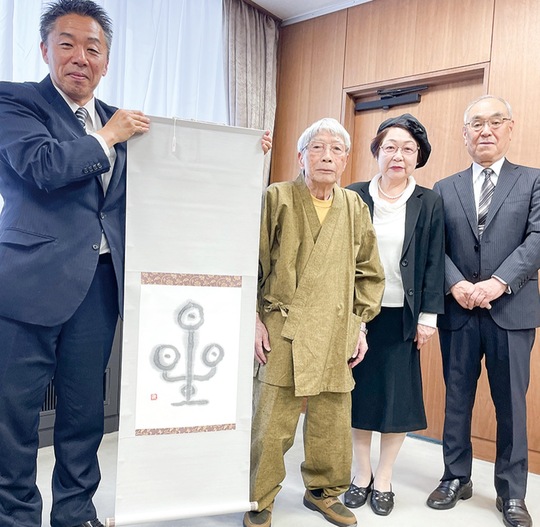 「星」と書かれた掛け軸を手にする古谷田市長と書道作品を手がけた竹内さん（左から２人目）＝７日・市長応接室で