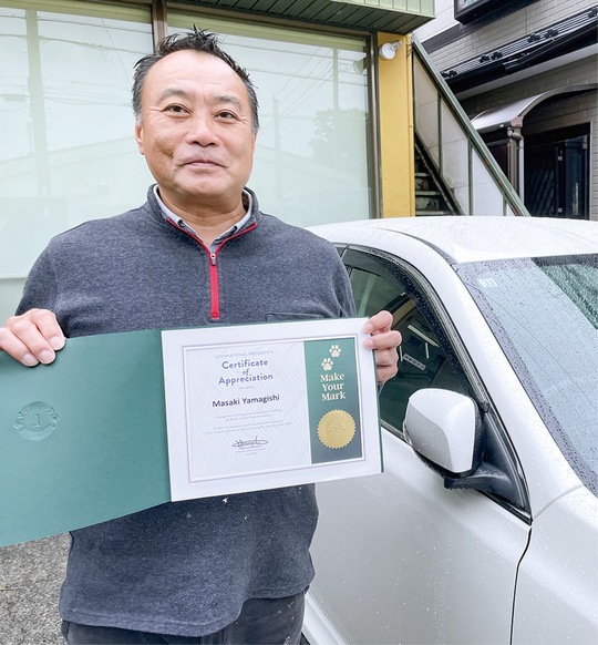 被災地へ向かう自家用車の前に立つ山岸さん＝5月30日