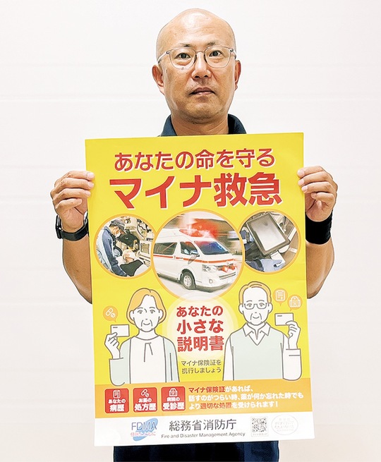 マイナ救急を知らせるポスターを持つ市消防救急救命課の内山穣課長