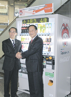 災害対応型自販機を前に握手する内野市長（左）と高橋社長（右）
