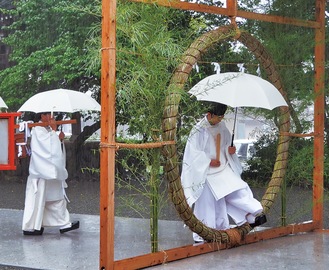 大雨の中、茅の輪をくぐる古木普総宮司（右）