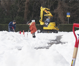 重機を用いての除雪作業にあたる市立図書館職員（２月19日撮影）