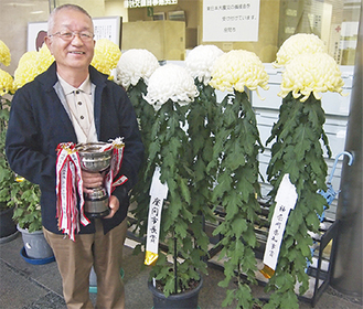 県知事賞と市長賞を獲得した作品の前でトロフィーを手にする大木さん