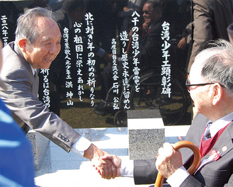 顕彰碑の前で固い握手を交わす、石川公弘会長（左）と李雪峰会長。顕彰碑には石川さんらが創作した３句が記されている