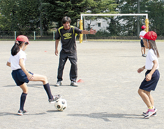 児童にボールの扱い方をアドバイスする松川さん（中央）