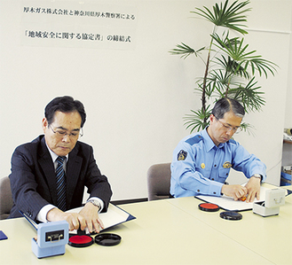 協定書に捺印する萱社長（左）と鈴木署長
