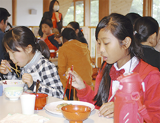 箸を使って給食のやきそばを食べるサラスワティ小学校の児童（右）
