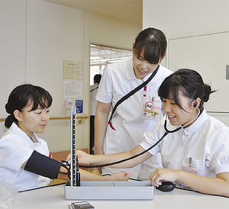 看護師（中央）から血圧計の使い方を教わる高校生