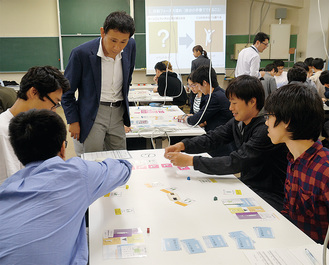ゲームを開発した講師の小野田純二さん（写真中央）のアドバイスを受けながらプレイする学生たち＝６月21日・東京工芸大厚木キャンパス