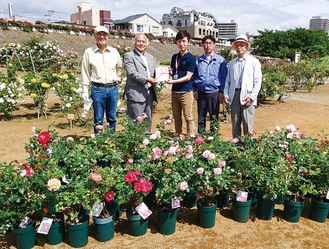寄贈されたバラ苗と目録を手渡す日本フルハーフ顧問の中野和辰さん（左から２番目）と、ローズガーデン関係者ら